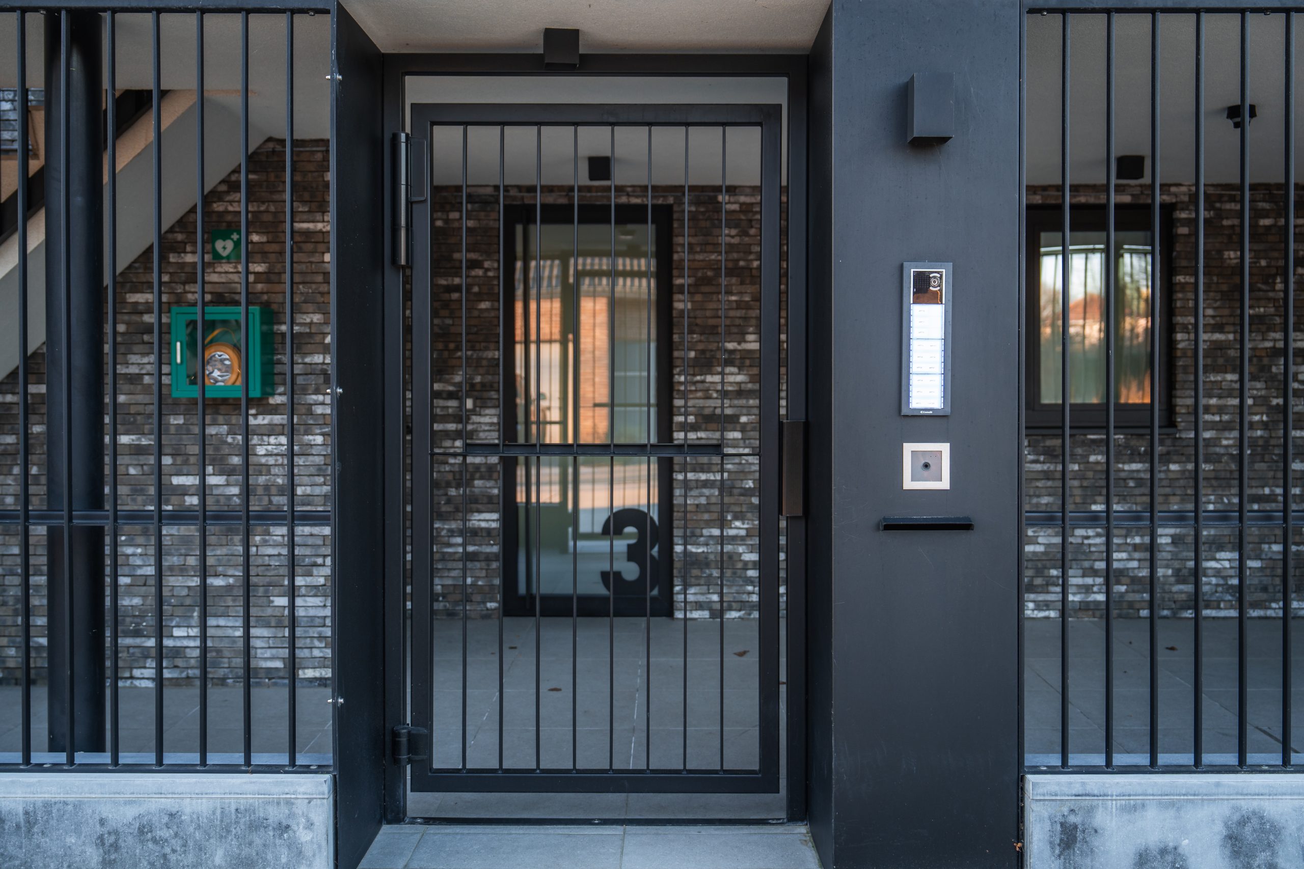 Aluminium inkomdeur met spijlen en parlofoon aan de gevel van een appartementsgebouw